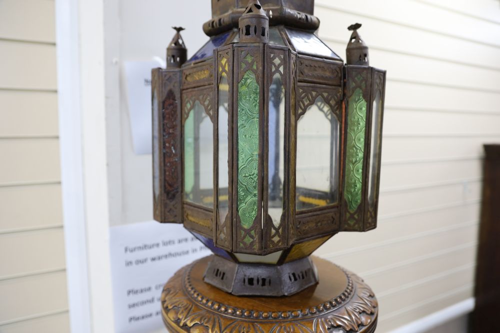 A pierced metal lantern with coloured glass panes, on carved walnut triform pedestal, 206cm overall